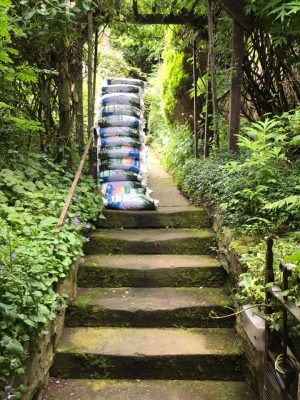 A pile of wood pallets at the top of a set of worn stone garden steps, with lots of lush greenery in a customer's garden - Wood Fuel Co-operative