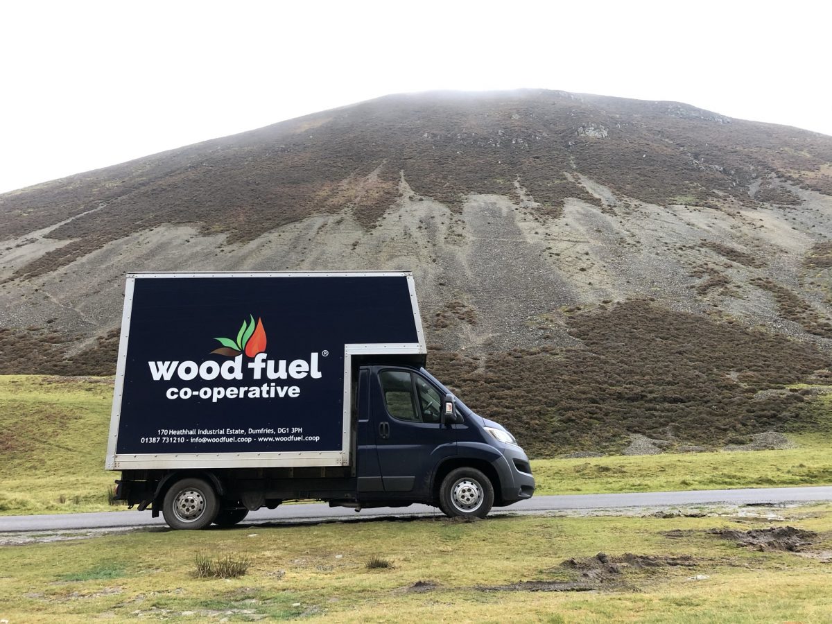 A blue Wood Fuel Co-operative van parked below dramatic misty hills - Wood Fuel Co-operative