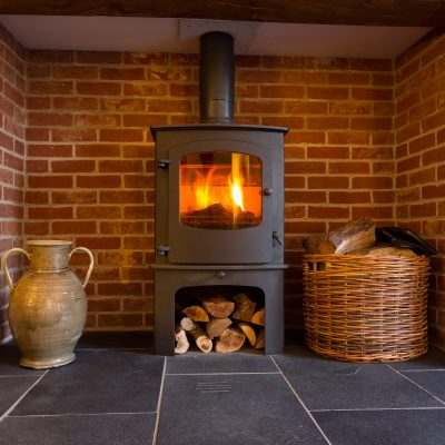 Roaring fire inside wood burning stove in brick fireplace with basket of cut wood ready for burning woodfuel cooperative